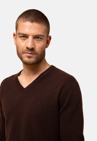 Br�ązowy sweter wełniany z dekoltem w serek o teksturowanym wykończeniu, cechujący się luźnym krojem oraz prążkowanymi detalami w okolicy kołnierza i dołu.