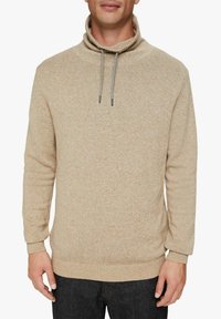 Pull en tricot beige à col roulé avec un cordon de serrage, des poignets et un ourlet côtelés. Présente un tissu texturé avec un motif subtil.