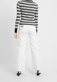 Białe dzwony z surowym wykończeniem na dole i beżową metką z tyłu. Połączone z dopasowaną czarno-szaro prążkowaną koszulą z długim rękawem.