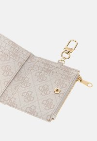 Portafoglio beige chiaro con motivo a rilievo del logo, hardware dorato e una tasca con zip. Presenta una clip per il fissaggio.