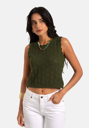 Grüner gestrickter Crop-Top mit Diamantmustern, gewellten Kanten und einer strukturierten Oberfläche, kombiniert mit weißen, hoch taillierten Hosen.