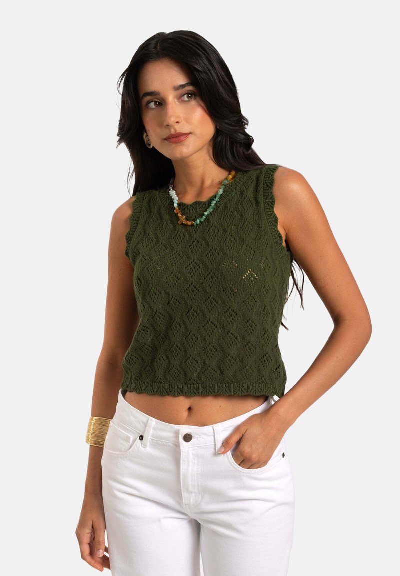 Grüner gestrickter Crop-Top mit Diamantmustern, gewellten Kanten und einer strukturierten Oberfläche, kombiniert mit weißen, hoch taillierten Hosen.