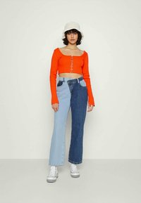 Top vermelho curto de mangas compridas com botões centrais, combinado com jeans flare bicolores (azul claro e azul escuro) e ténis brancos.