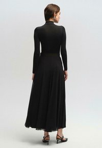 Vestido negro de manga larga con un corpiño ajustado y falda fluida, hecho de una tela suave, con una cintura definida y dobladillo hasta los tobillos.