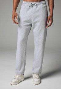 Graue Jogginghosen mit einem lockeren Schnitt, elastischem Taillenbund, Seitentaschen und Kordelzug. Kombiniert mit beigen Sneakers.
