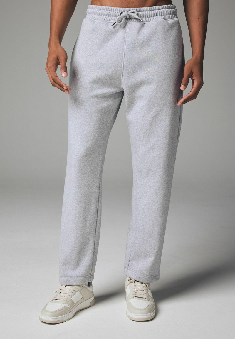 Graue Jogginghosen mit einem lockeren Schnitt, elastischem Taillenbund, Seitentaschen und Kordelzug. Kombiniert mit beigen Sneakers.