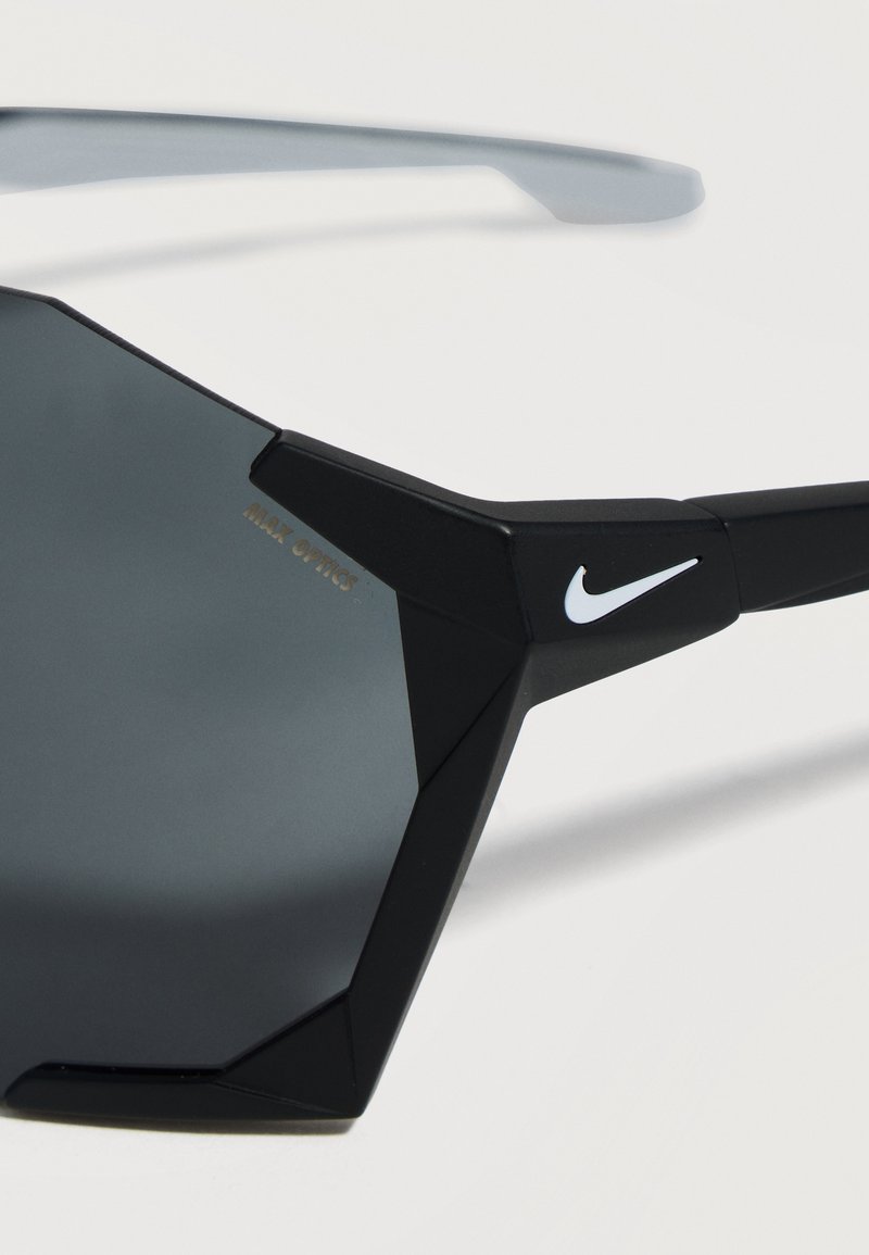 Schwarze eckige Nike Sport-Sonnenbrille mit dunklen Gläsern und weißem Logo am Bügel, vor weißem Hintergrund gezeigt.