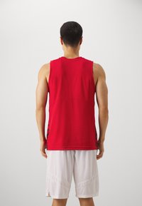 Top atlético rojo sin mangas con un acabado texturizado y patrones laterales. Combinado con pantalones cortos de malla blancos, que presentan un corte holgado y costuras decorativas.