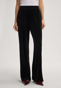 Zwarte wijde broek gemaakt van zacht textiel met een gladde structuur, voorzien van een hoge tailleband en zijzakken. Gecombineerd met bordeauxrode schoenen.