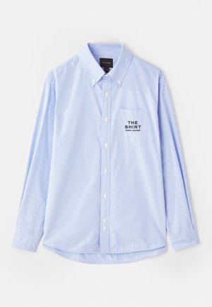 Svetlo modra srajca z gumbi, z verticalnimi belimi črtami, dolgimi rokavi, ovratnikom s gumbi in žepom na prsih, ki vsebuje napis "THE SHIRT".
