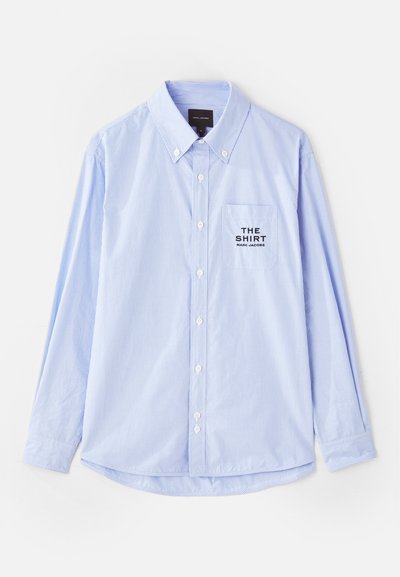 Cămașă albastru deschis, cu dungi verticale albe, mâneci lungi, guler cu nasturi și un buzunar pe piept cu textul "THE SHIRT".