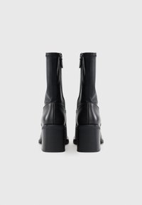 Μαύρες δερμάτινες μπότες μέχρι τον αστράγαλο με κομψό σχέδιο, που διαθέτουν φερμουάρ στην πίσω πλευρά και χοντρό, υφασμάτινο τακούνι.