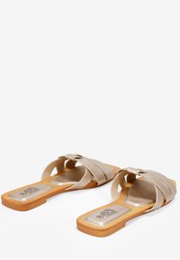 Sandales ouvertes beiges avec des lanières croisées, semelle plate et semelle intérieure métallique. Présente un design minimaliste et une texture lisse.
