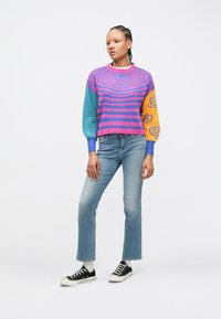 Krāsains adīts džemperis ar rozā un zilām svītrām, kā arī oranžām piedurknēm ar virpuļveida rakstiem. Sapārots ar gaiši zilām džinsa biksēm un melniem sporta apaviem.