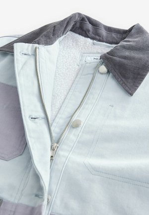 Giubbotto di jeans azzurro chiaro con colletto in corduroy, zip argentata e fodera morbida e testurizzata. Decorato con toppe di tessuto a contrasto.