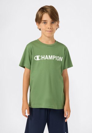 Groene katoenen T-shirt met ronde hals en korte mouwen, met een witte "CHAMPION"-logo gedrukt op de voorkant. Draagt bij een marineblauwe short.