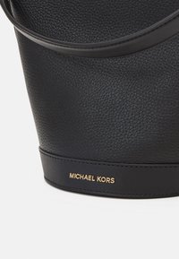 Schwarzlederne Handtasche mit strukturiertem Finish. Sie hat eine abgerundete Form, einen kurzen Henkel und ein goldenes "MICHAEL KORS"-Logo an der Basis.