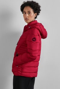 Rote gepolsterte Jacke mit Kapuze, versehen mit horizontaler Steppung, einem Logo-Patch am Arm und mit Reißverschlüssen versehenen Taschen. Glatte Textur und strapazierfähiges Material.