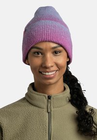 Gorro de punto con un patrón degradado en púrpura y rosa. Textura suave, diseño de pico, borde acanalado, combinado con una chaqueta de forro polar verde.