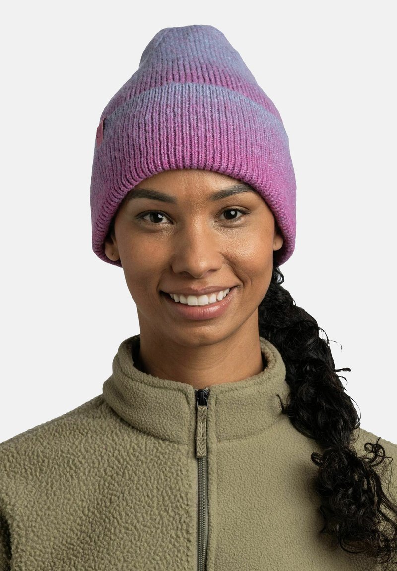 Gorro de punto con un patrón degradado en púrpura y rosa. Textura suave, diseño de pico, borde acanalado, combinado con una chaqueta de forro polar verde.