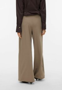 Højttaljede bukser med vide ben i et blødt, afdæmpet beige stof med en glat tekstur og rene linjer, kombineret med en mørk bluse.