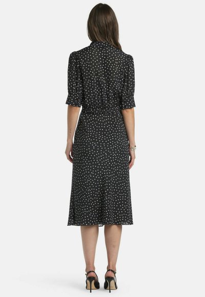 Črna obleka s kratkimi nabranimi rokavi, poudarjenim pasom in belimi pikami. Ohlapen krilo do sredine meč, teksturirana tkanina, čevlji s paščkom ob gležnju.