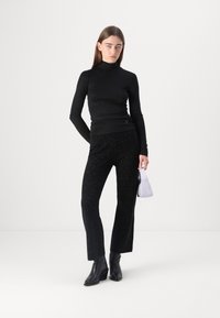 Pull noir à manches longues en col roulé, ajusté ; pantalon noir avec des paillettes discrètes, coupe droite ; bottes noires hauteur cheville ; petit sac à main lavande.