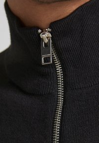 Maglione zip-up nero con una texture a coste, dotato di una cerniera argento e un tirante contrassegnato "JACK & JONES." Design con colletto alto.