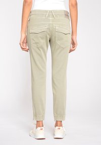 Ljusgröna, avsmalnande byxor med en elastisk midja, två bakfickor och elastiska muddar, tillsammans med vita sneakers med orange detaljer.