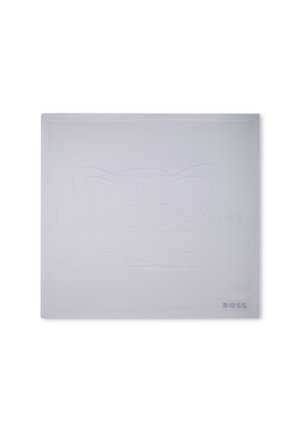 Manta blanca con un diseño texturizado en relieve de una cara de dibujos animados, con un borde acanalado y un logo discreto en la esquina.