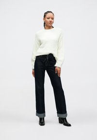 Hvit, strukturert genser med lange ermer, kombinert med mørke, høytlivede denimjeans med blomsterbelte og oppbrettede kanter. Svarte ankelstøvler.