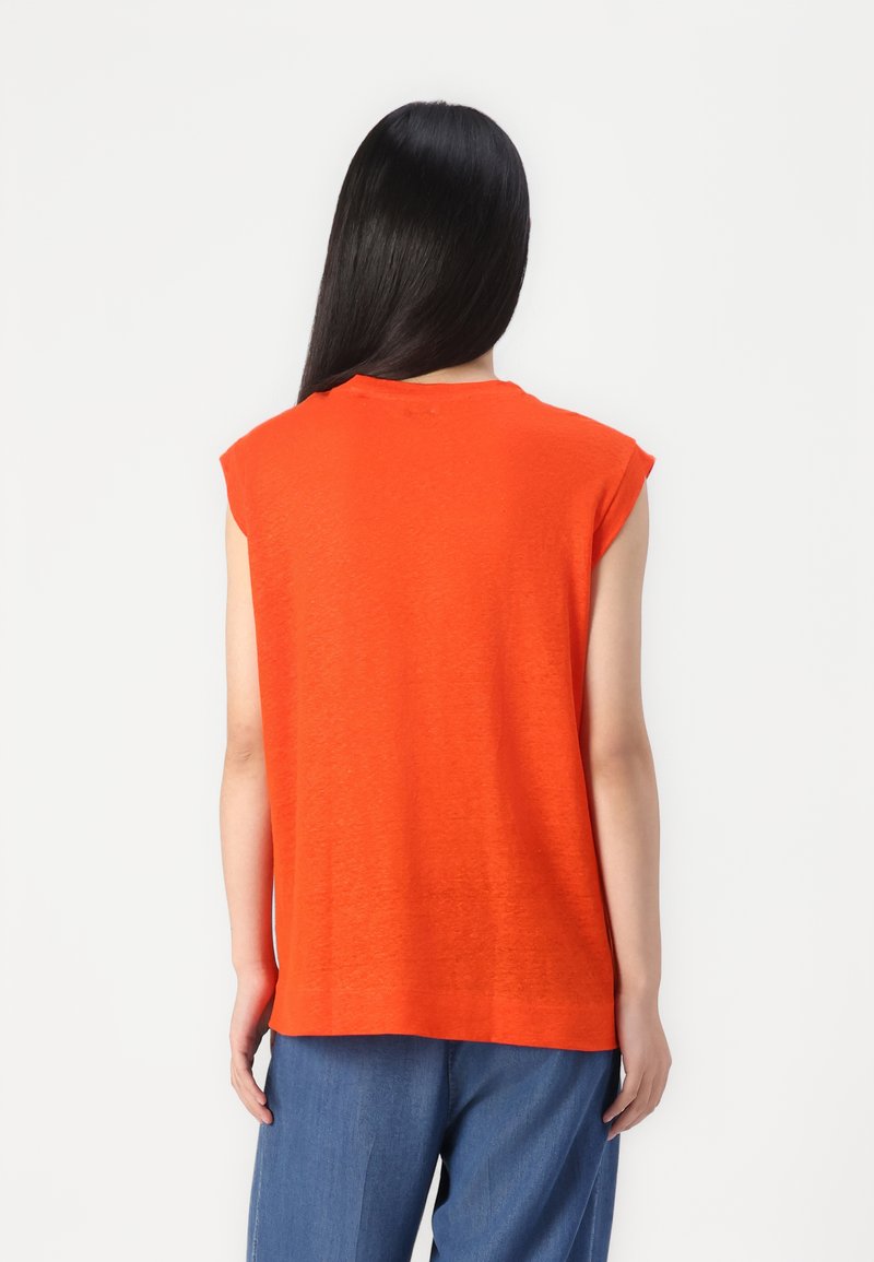 Haut en tricot orange sans manches avec une coupe décontractée, présentant un col rond et des épaules légèrement abaissées, associé à un pantalon bleu à jambes larges.
