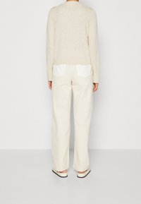 Maglione beige con maniche lunghe, orlo a coste e lavorazione a maglia testurizzata. Abbinato a pantaloni a gamba larga color crema con tasche posteriori bianche e scarpe basse.