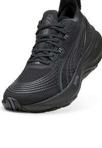 Black running shoe with a textured mesh upper, prominent lacing system, and cushioned sole. Features subtle branding and streamlined design.