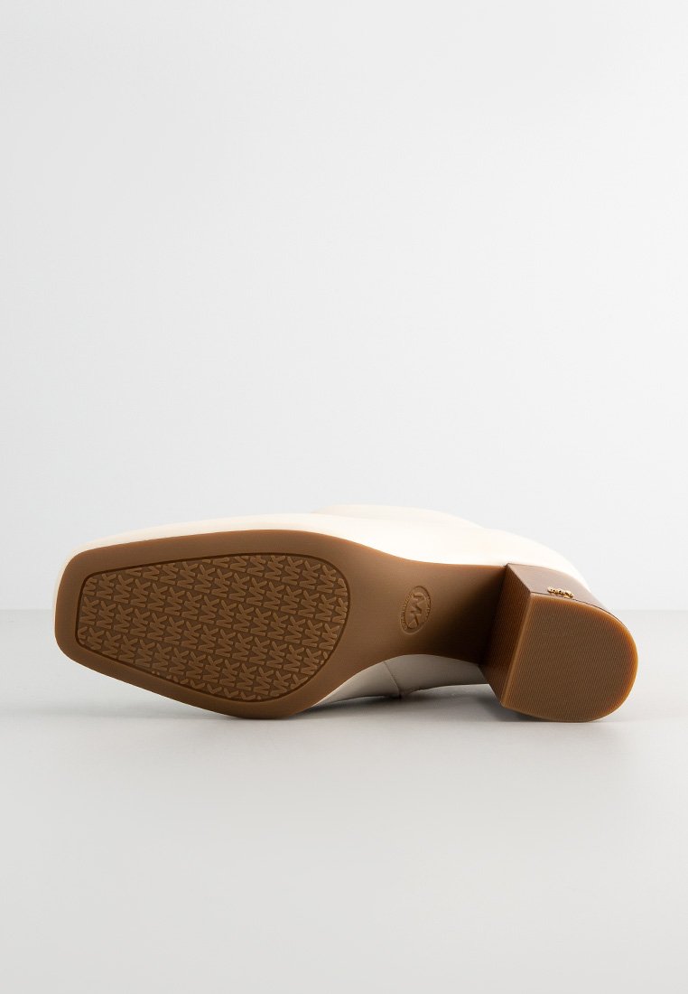 Stivale bianco con tacco posato di lato che mostra una suola marrone testurizzata e un tacco a blocco su uno sfondo uniformemente chiaro.