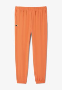 Pantaloni sportivi arancioni con cintura elastica, tasche laterali e un accento logo verde. Il materiale appare liscio e leggero.