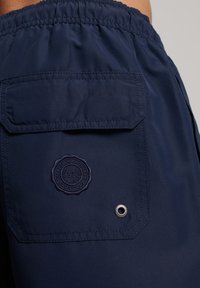 Shorts blu navy realizzati in tessuto leggero, dotati di una vita elasticizzata, di una tasca posteriore con patch logo e di un dettaglio con occhiello metallico.