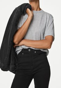 Camiseta gris de manga corta combinada con jeans negros de cintura alta. Una chaqueta de mezclilla negra está colgada sobre un hombro.