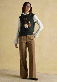 Tumši zaļš adīts bez piedurknēm ar lapsas dizainu; pārklāts ar baltu, viļņotu blūzi. Brūnas svītrainas bikses ar plašām kājām un smalku tekstūru.