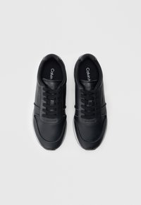 Μαύρα αθλητικά παπούτσια με λείο συνθετικό άνω μέρος, στρογγυλή μύτη και επίπεδα κορδόνια. Διαθέτουν λευκή ελαστική σόλα και λογότυπο "Calvin Klein" στη σόλα του παπουτσιού.