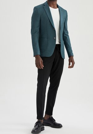 Teal wollen blazer met ingezette revers, twee voorzakken, enkele knoopsluiting, gecombineerd met zwarte tapered broek en zwarte schoenen.