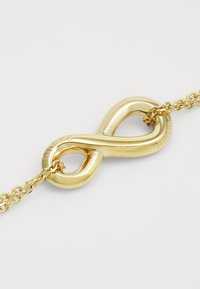 Bracciale infinito tono oro con una finitura metallica liscia, caratterizzato da un design a loop intrecciato e dettagli di catena interconnessi.