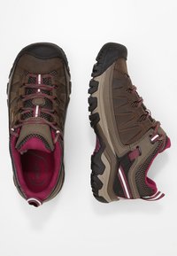 Braune Wanderschuhe mit einem Obermaterial aus Mesh, burgunderfarbenen Akzenten, strukturiertem Gummisohlen und kontrastierenden weißen Streifen an der Seite.