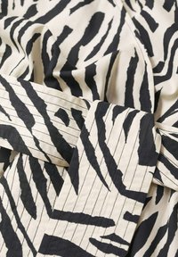 Tissu à imprimé zèbre noir et blanc avec une texture lisse. Comprend des rayures épaisses et fines, des sections pliées, et des fines rayures horizontales sur la ceinture.