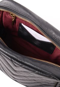 Bolsa de cuero negro con exterior acolchado, cremallera dorada y forro burdeos; cuenta con un bolsillo interno para tarjetas con una tarjeta dentro.