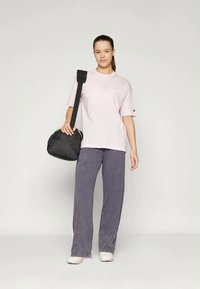 Ružový bavlnený tričko, voľný strih, krátke rukávy; spárované so svetlo fialovými širokými nohavicami a čiernou kabelkou cez plece; minimalistický dizajn.