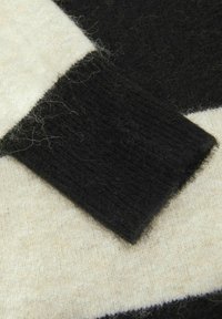 Tessuto lavorato a maglia nero e crema, con una texture morbida. Presenta colori a contrasto in blocchi, con una leggera peluria sulla superficie.