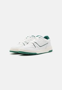 Zapatillas blancas de cuero y malla con acentos verdes. Las características incluyen una lengüeta acolchada, un panel lateral texturizado y una suela de goma.