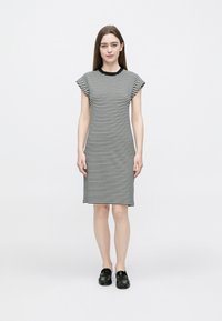 Zwart-wit gestreepte jurk met korte mouwen, tot op de knie, met een ronde halslijn. De stof oogt zacht en licht getailleerd. Zwarte platte schoenen.