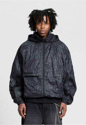 Schwarze, zerknitterte Stoffjacke mit Kapuze, Frontreißverschluss, elastischen Bündchen und einer großen Fronttasche. Detaillierte Textur und lockere Passform.